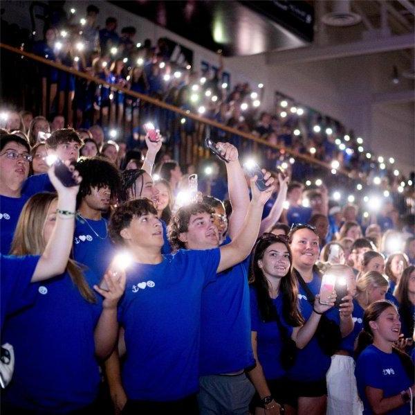 students in blue tshirts standing holding cell phones with lights on